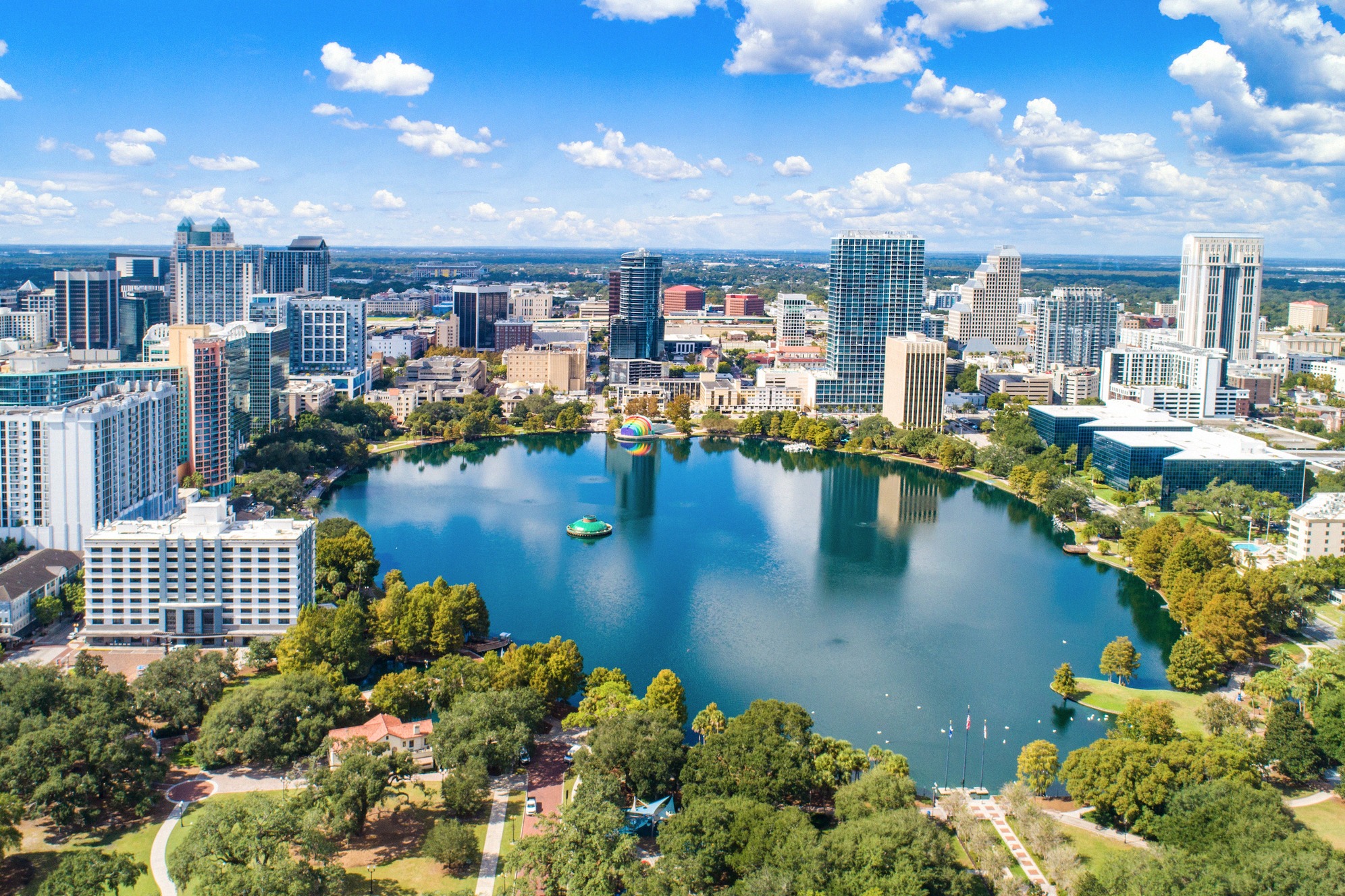 Ilmapanoraama Orlandon keskustasta Floridassa: smaragdinvihreä Lake Eola amfiteattereineen heijastaa keskustan pilvenpiirtäjiä sinisen Floridan taivaan alla.