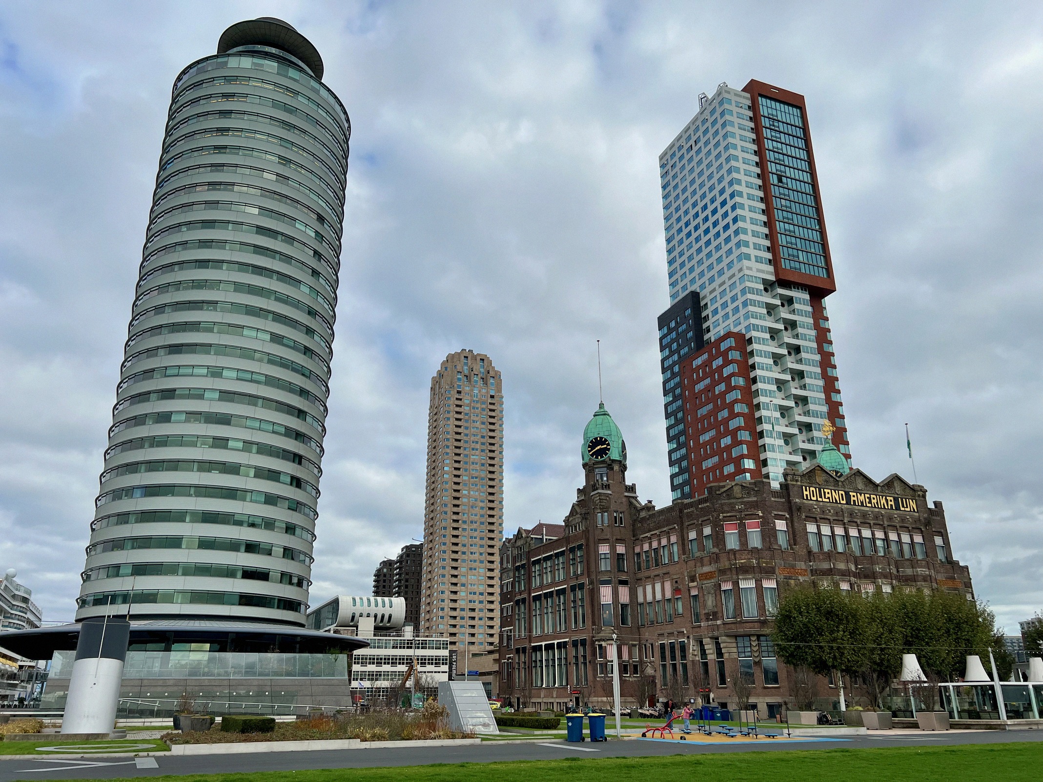 Kontrastikas silhuetti Rotterdamin Wilhelminapierillä, oikealla entisen Holland-Amerika-Lijnin punatiilinen rakennus vihreine kupoleineen (nykyään Hotel New York), ympärillä moderneja pilvenpiirtäjiä, muun muassa hoikka World Port Center. Kuva näyttää Rotterdamin satamahistorian ja nykyarkkitehtuurin yhdistelmän.