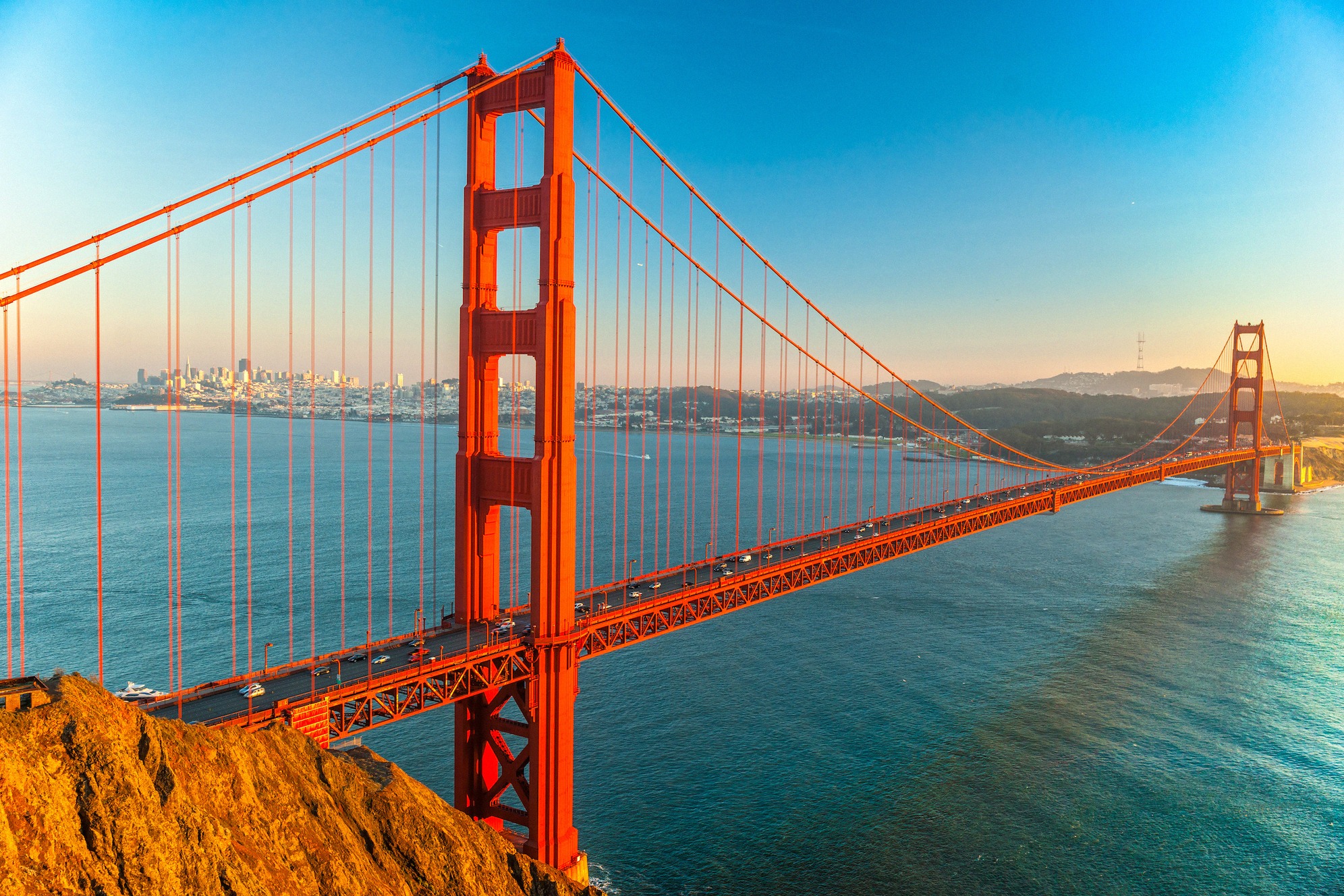 Golden Gate Bridge lämpimässä iltavalossa Marin Headlandsilta kuvattuna, taustalla San Franciscon utuinen silhuetti.