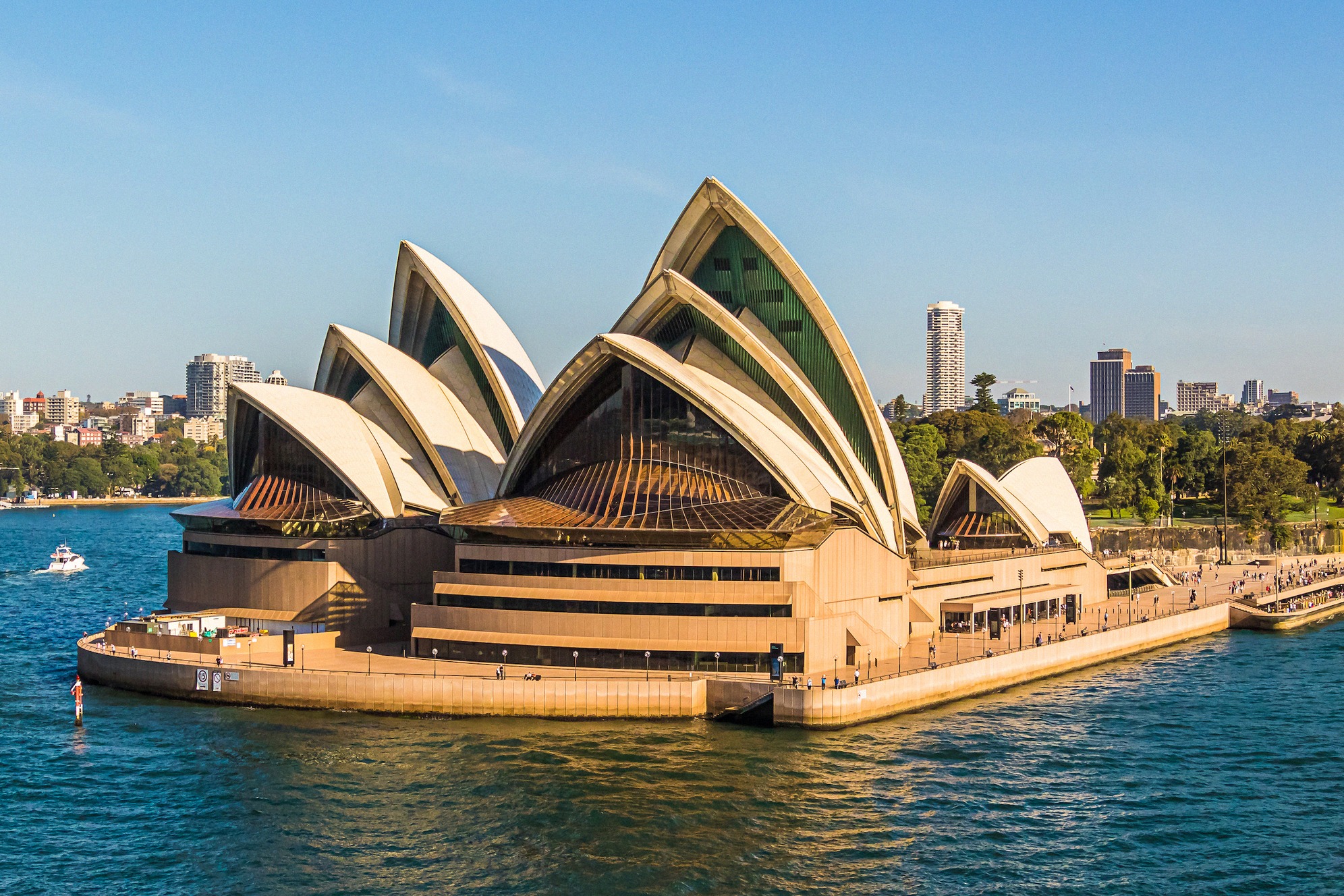Sydneyn oopperatalo vedeltä kuvattuna, valkoiset kuorikatot ja pilvenpiirtäjät taustalla.