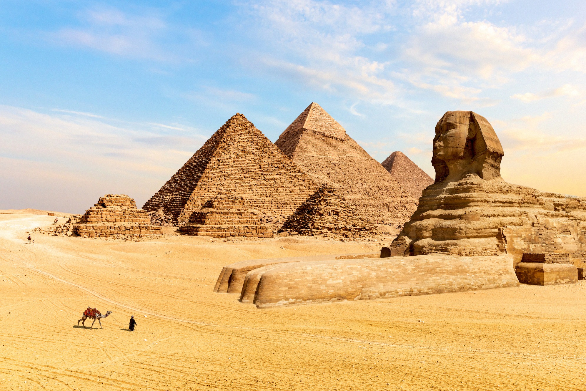 Gizan kolme pyramidia ja suuri sfinksi kultaisella aavikkohiekalla, Egyptin tunnetuin maamerkki, edessä kameli ja ratsastaja.