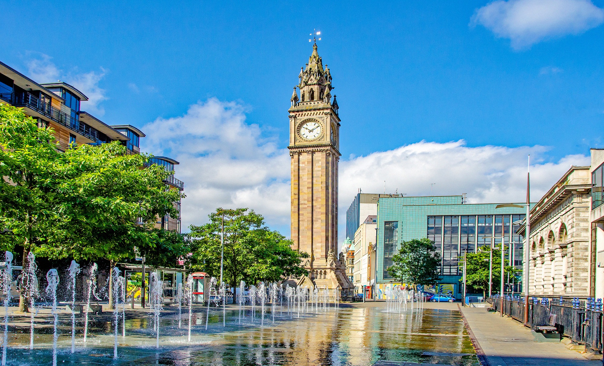 Viktoriaaninen Albert Memorial Clock Tower Belfastissa, etualalla vesisuihkuja ja taustalla moderneja rakennuksia