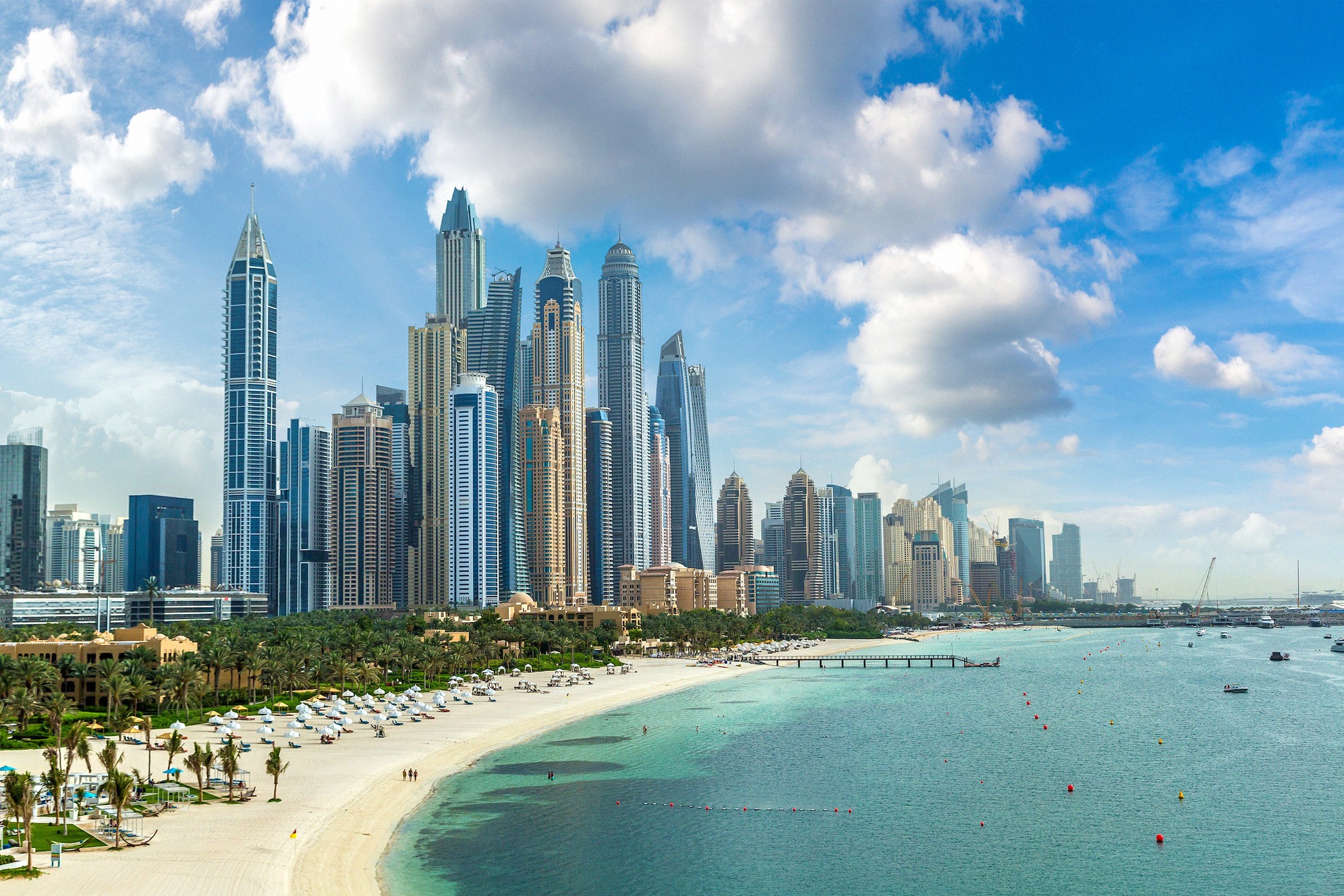 Dubai Marinan tornitalot hiekkarannalta turkoosin veden yli katsottuna.