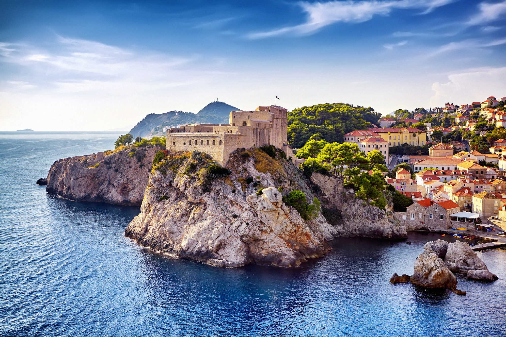 Lovrijenacin linnoitus jyrkästi laskevalla kalliolla meren äärellä, kuvattuna Dubrovnikin kaupunginmuureilta. Keskiaikainen linnoitus Adrianmeren yllä ja vanhakaupunki taustalla kultaisessa iltavalossa.