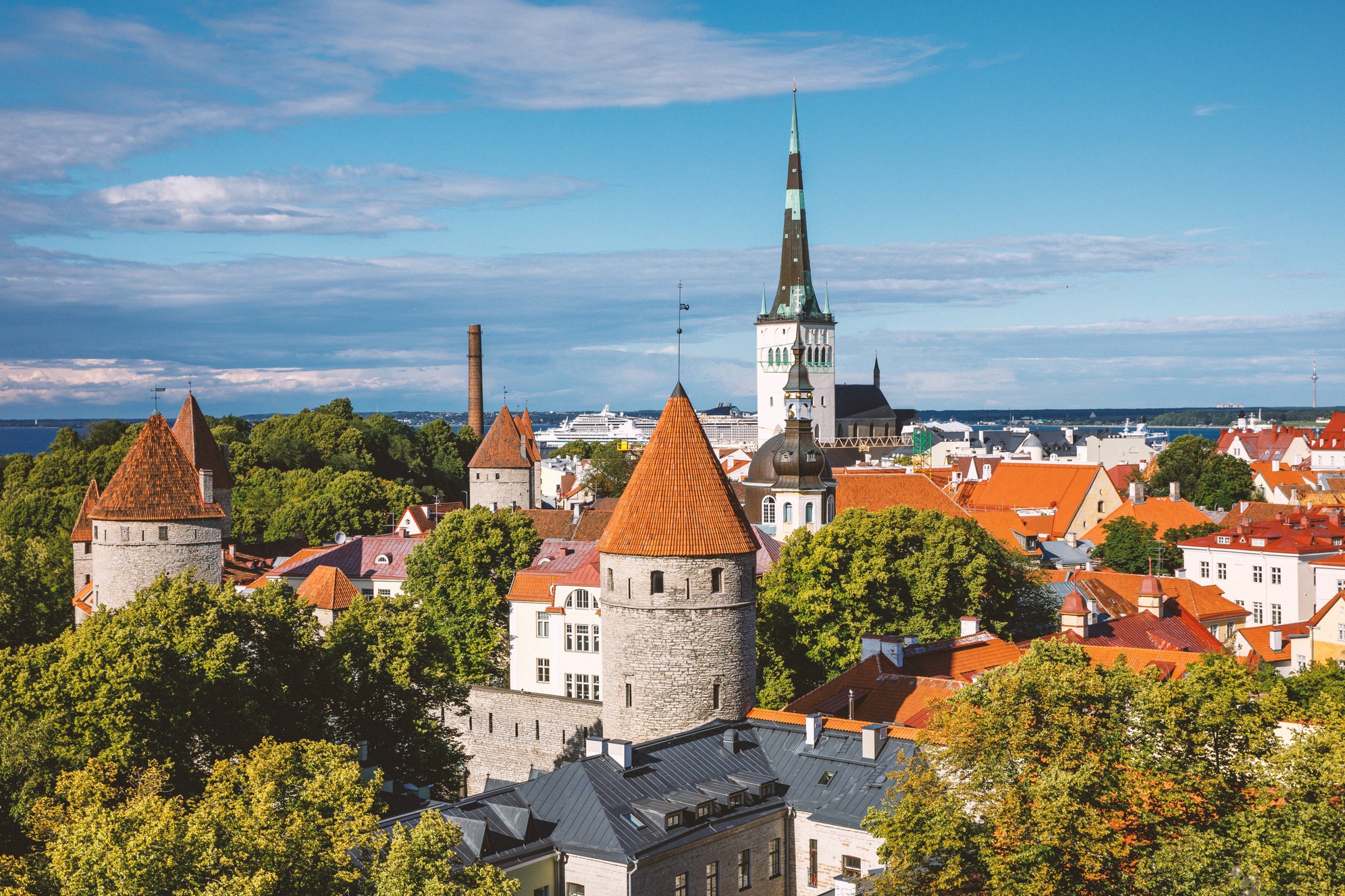 Panoraamanäkymä Tallinnan keskiaikaiseen vanhaankaupunkiin kaupunginmuurin tunnusomaisten asuintornien ja Oleviste-kirkon näyttävän tornin kanssa kesällä.