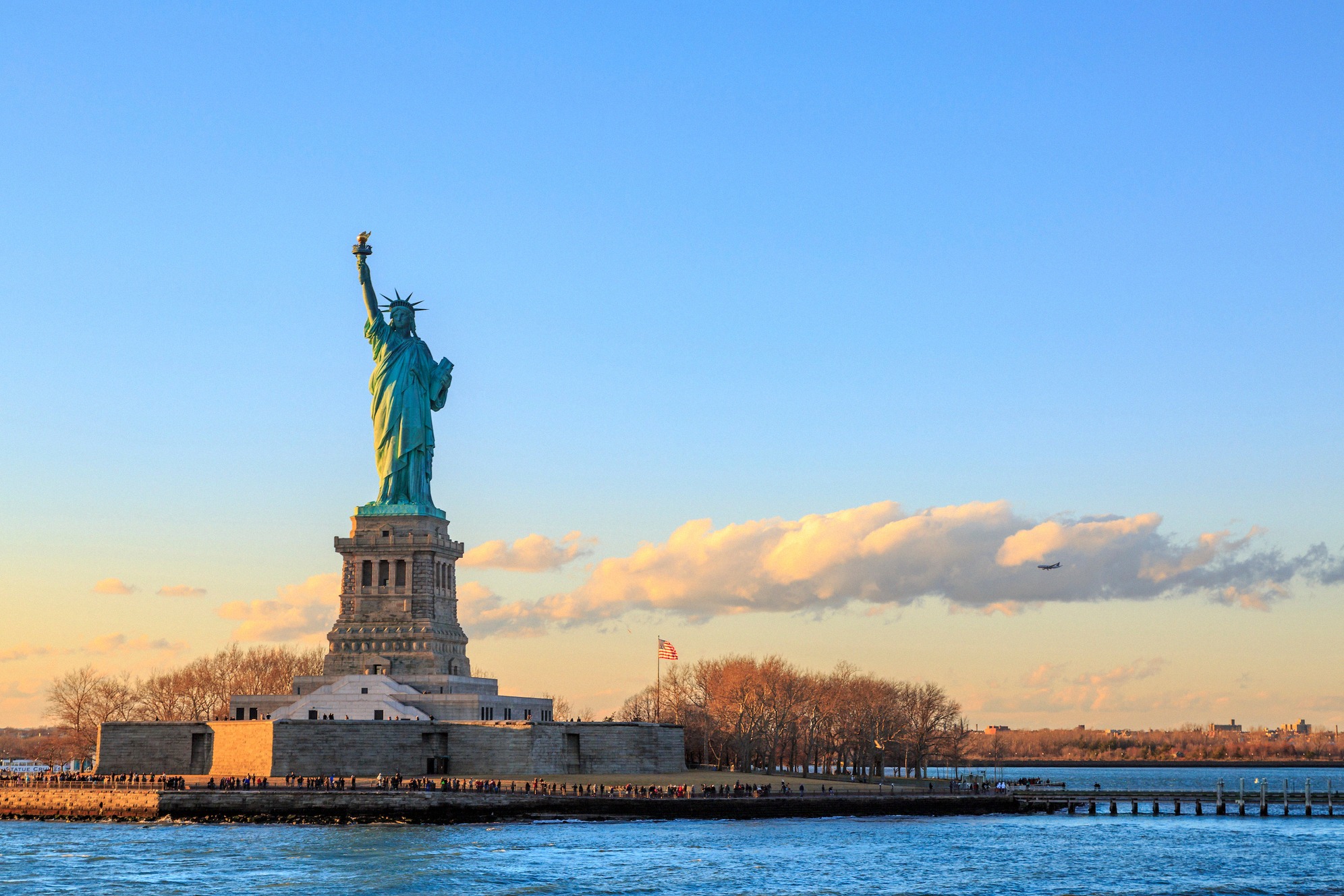 Vapaudenpatsas Liberty Islandilla auringonlaskun valossa. Yhdysvaltain tunnus kohoaa mahtavana New Yorkin satamassa, taustalla New Jerseyn rannikko.