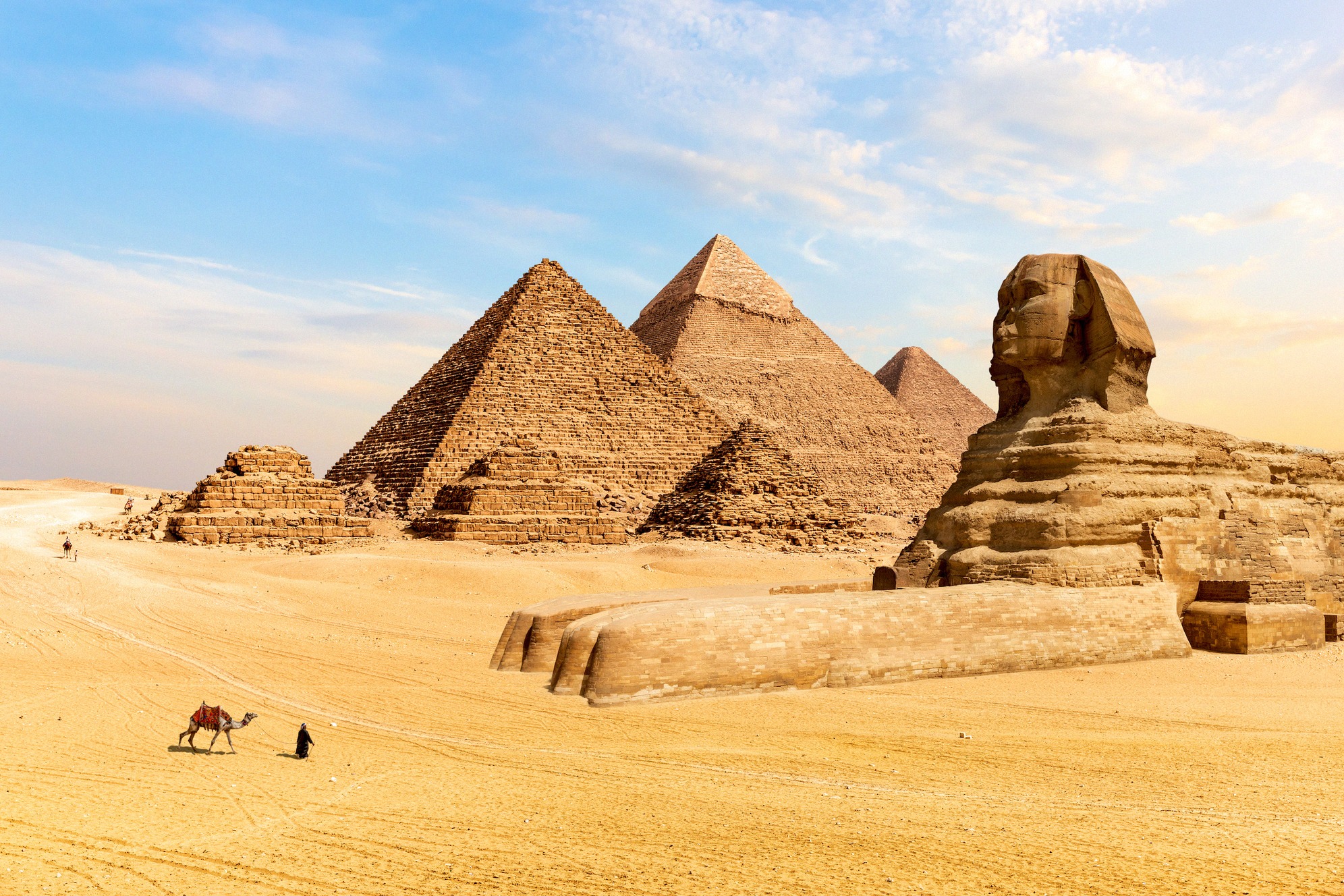 Gizan kolme pyramidia ja Suuri sfinksi kultaisessa aavikkohiekassa, Egyptin kuuluisin maamerkki, etualalla kameli ja ratsastaja.