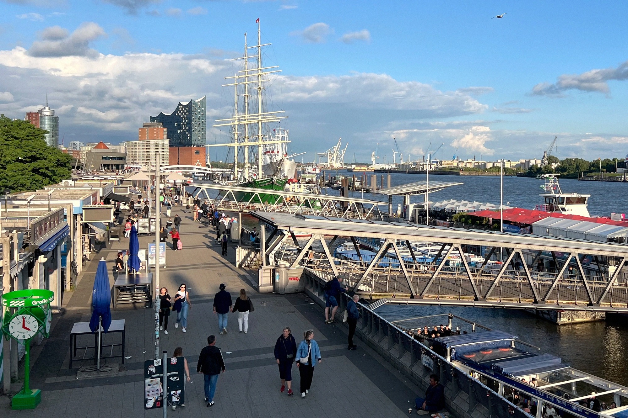 Elbphilharmonie vedestä kuvattuna: kaareva lasiosa punatiilisen Kaispeicher-varaston päällä, vieressä Unilever-talo, sininen taivas ja pilviä.
