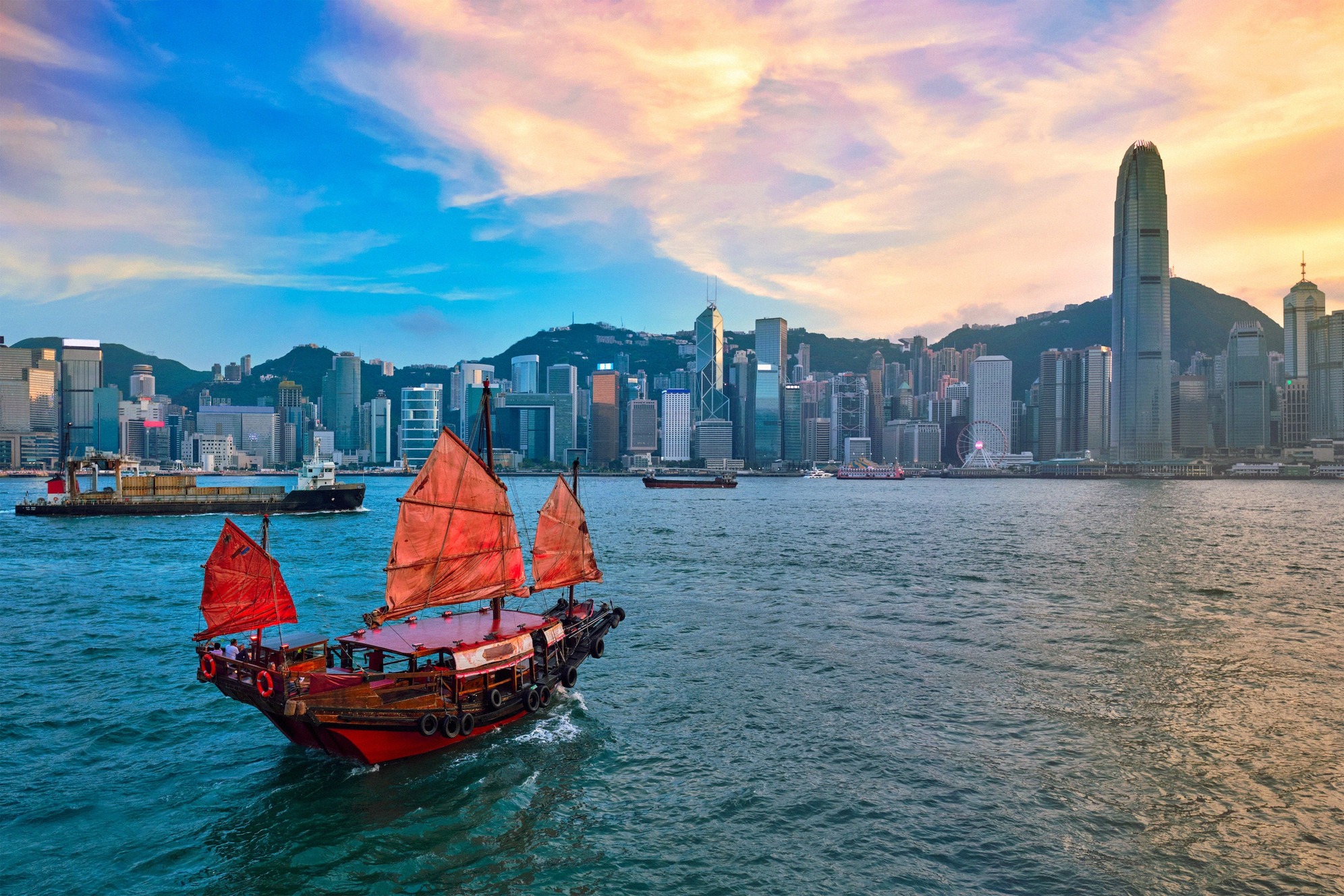 Kiinalainen punapurjeinen džonkki Victoria Harbourilla Hongkongin pilvenpiirtäjien edessä.