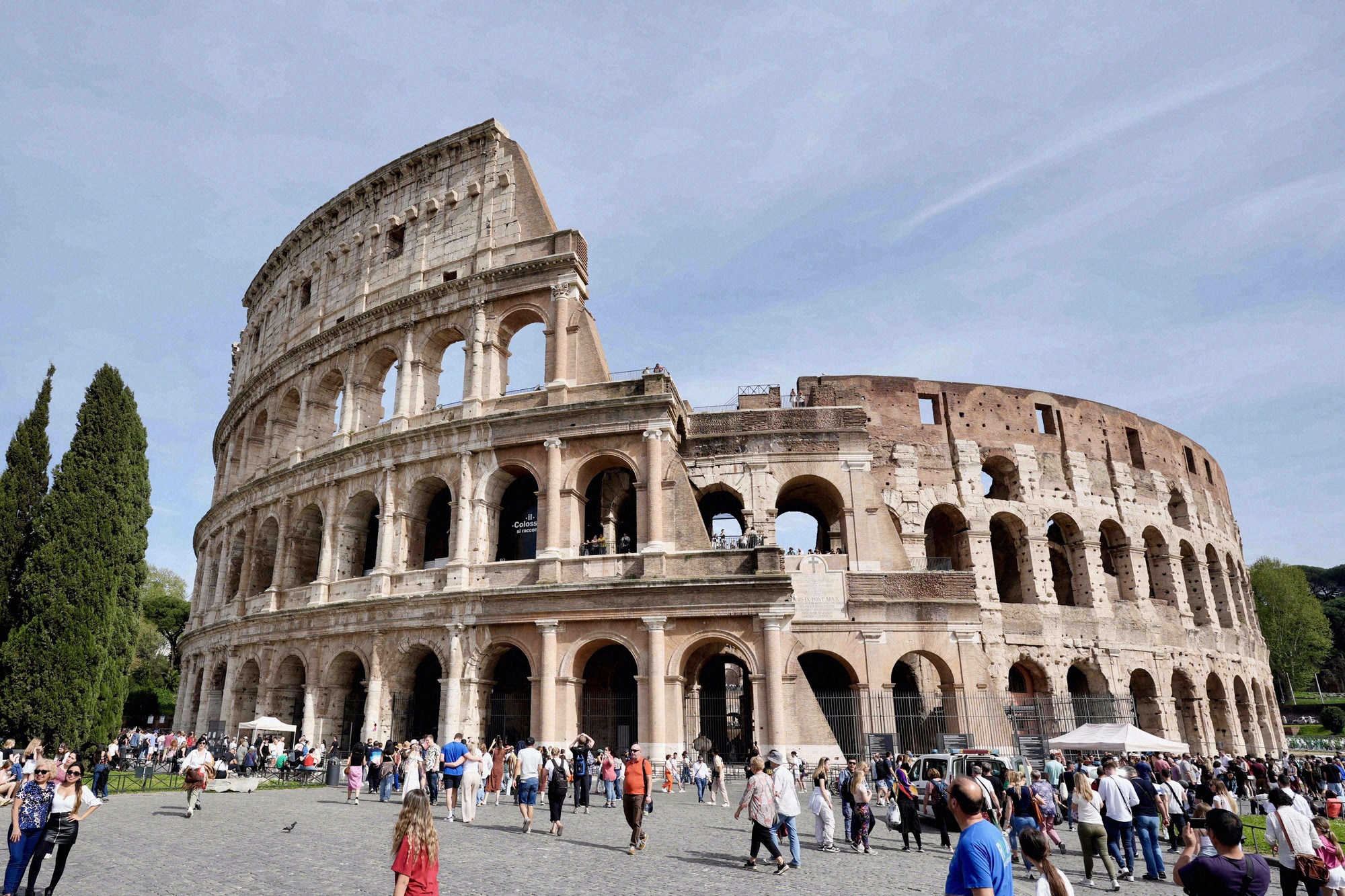Rooman Colosseum ulkoa: kaarikäytävien kerrokset kohoavat aukiolla kulkevien kävijöiden yllä.
