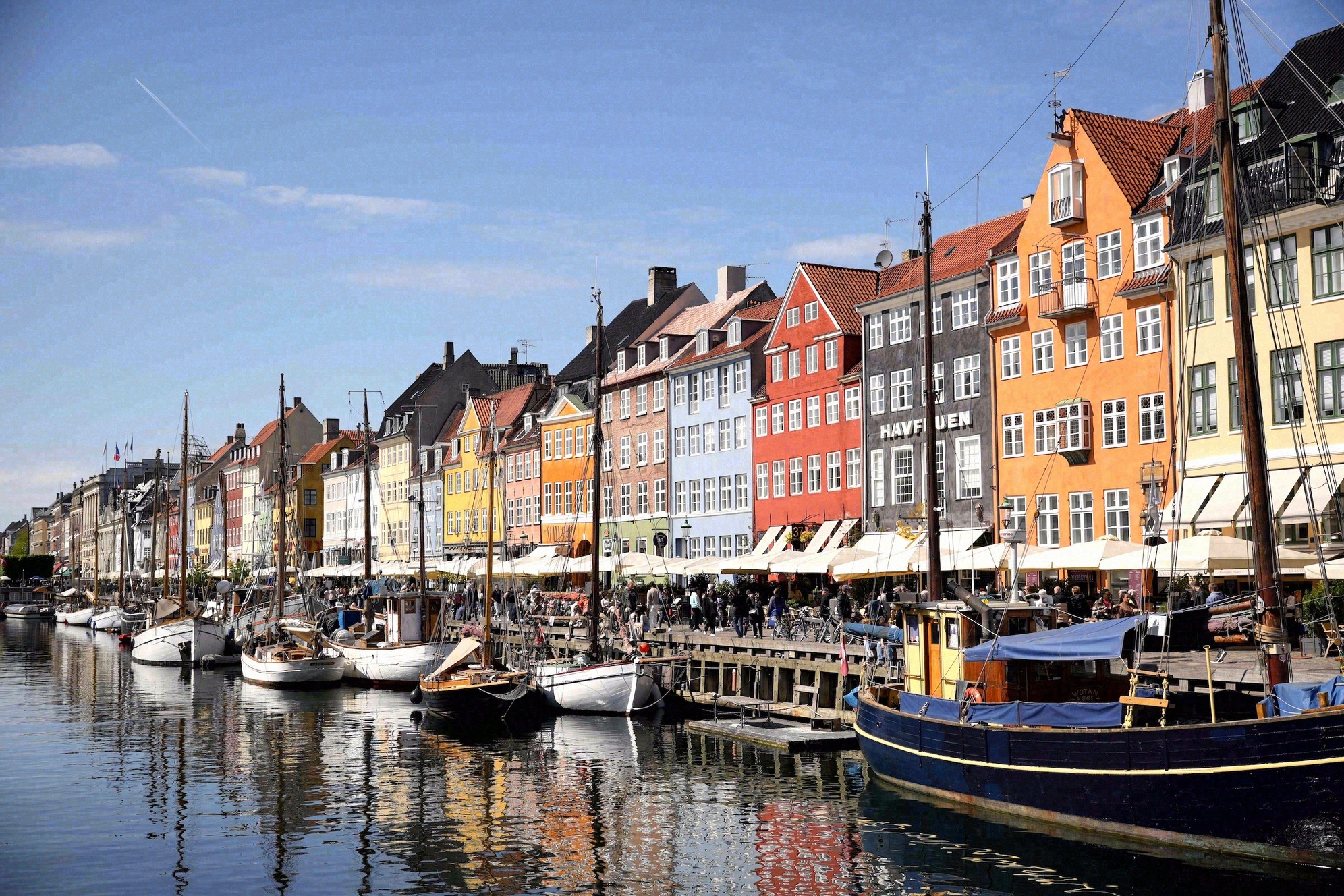 Nyhavn Kööpenhaminassa: kuuluisa satamakanavanäkymä punaisine, keltaisine, okrankeltaisine ja sinisine porvaristaloineen, edessä historiallisia puulaivoja ja veneitä laitureissa. Tanskan pääkaupungin suosittu maamerkki.