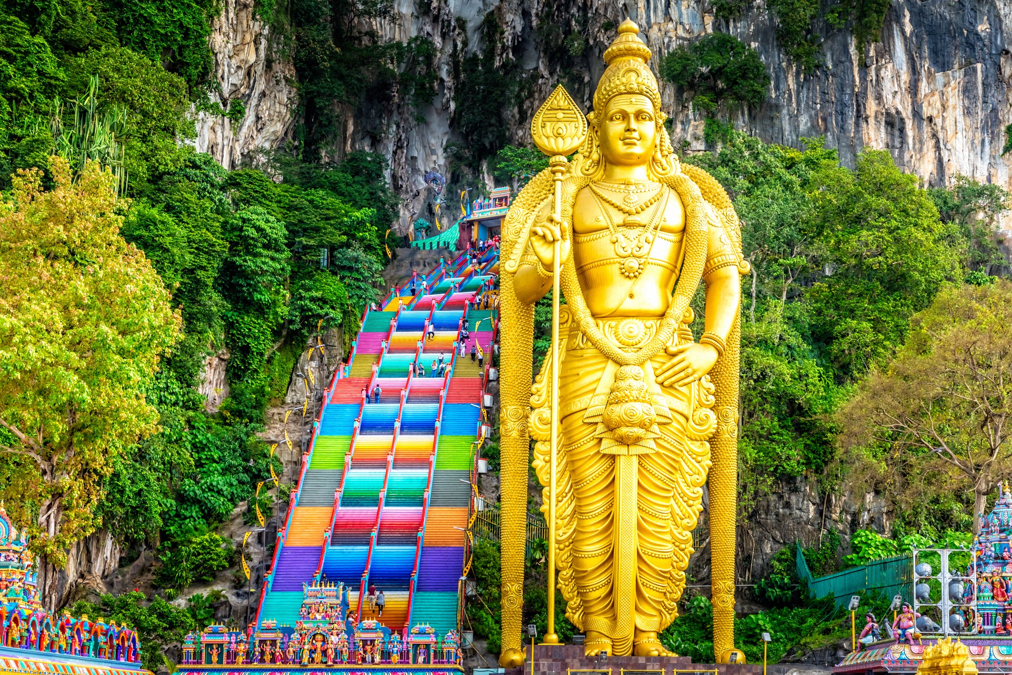 Kultainen Murugan-patsas Batun luolien edessä Kuala Lumpurin lähellä ja värikkäät portaat ylös kalkkikiviluolaan.