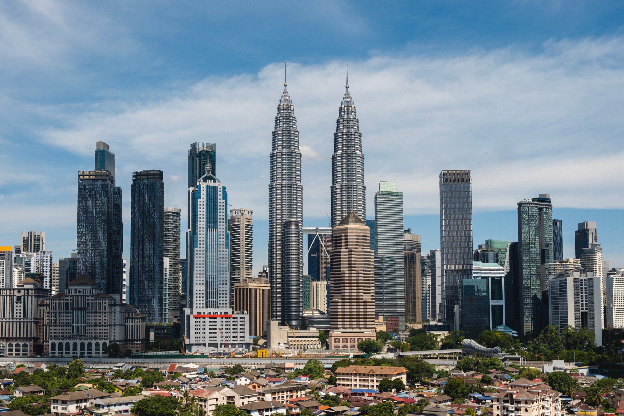 Kuala Lumpurin näyttävä silhuetti, jonka keskipisteenä ovat ikoniset Petronas-kaksoistornit. Lukuisat pilvenpiirtäjät muodostavat Malesian pääkaupungin modernin kaupunkikuvan sinistä taivasta vasten.