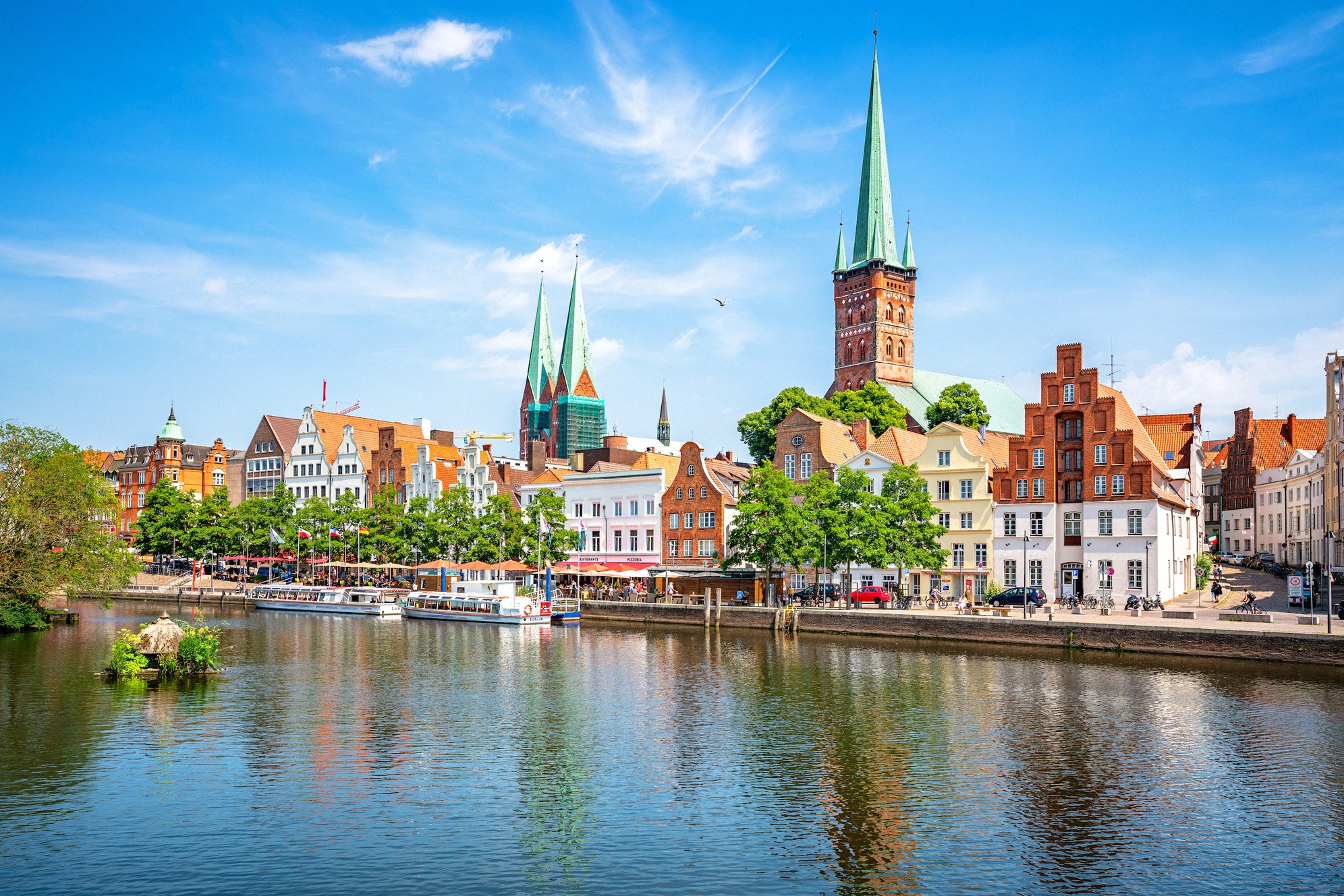 Klassinen panoraamanäkymä Lübeckin vanhaankaupunkiin Trave-joelta, näyttävinä Marienkirchen ja Petrikirchen tornit. Hansa-ajan porvaristalot heijastuvat vedestä.