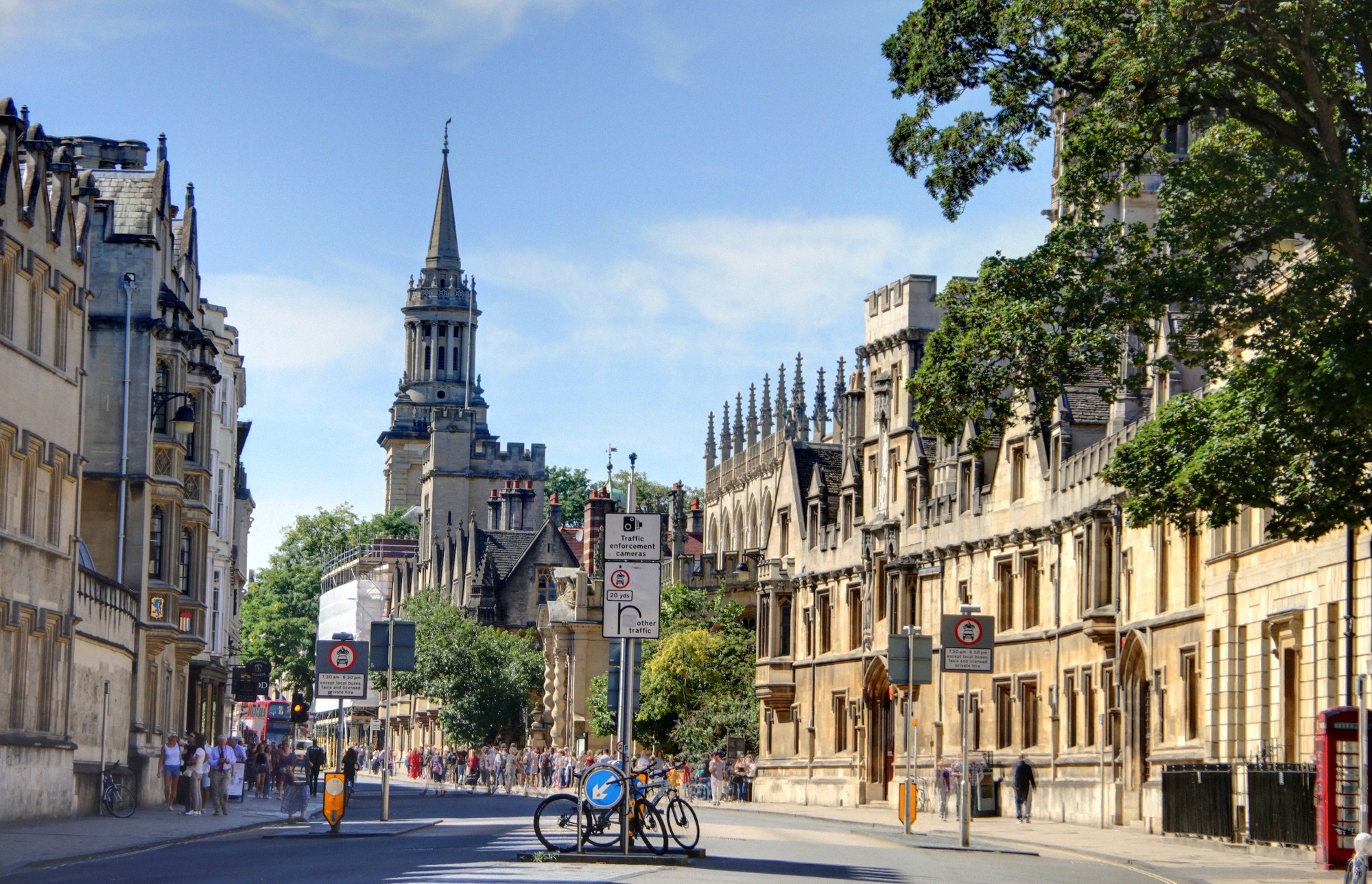 Oxfordin historiallinen High Street goottilaisine yliopistorakennuksineen, vilkas katuelämä ja punainen puhelinkoppi.