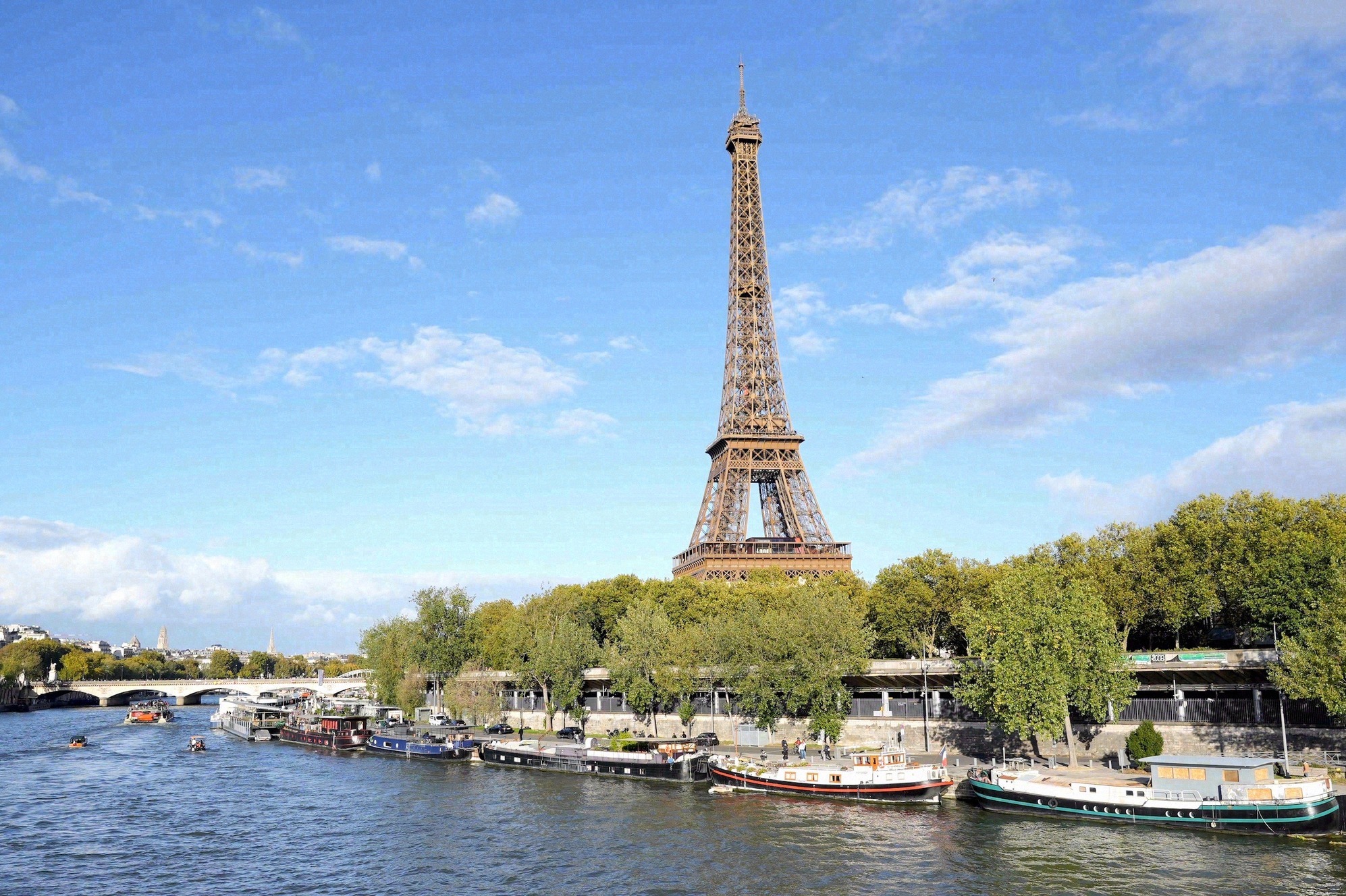 Näkymä Eiffel-torniin Seineltä, etualalla asuntolaivoja ja silta.