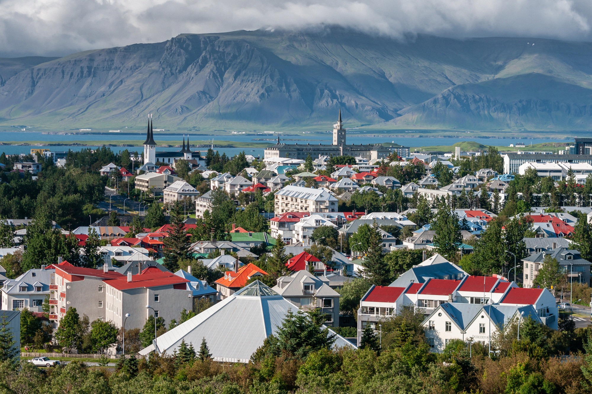 Laaja kaupunkipanoraama Reykjavíkista värikkäine kattoineen, kirkontorneineen ja Islannin lumihuippuisine vuorineen taustalla