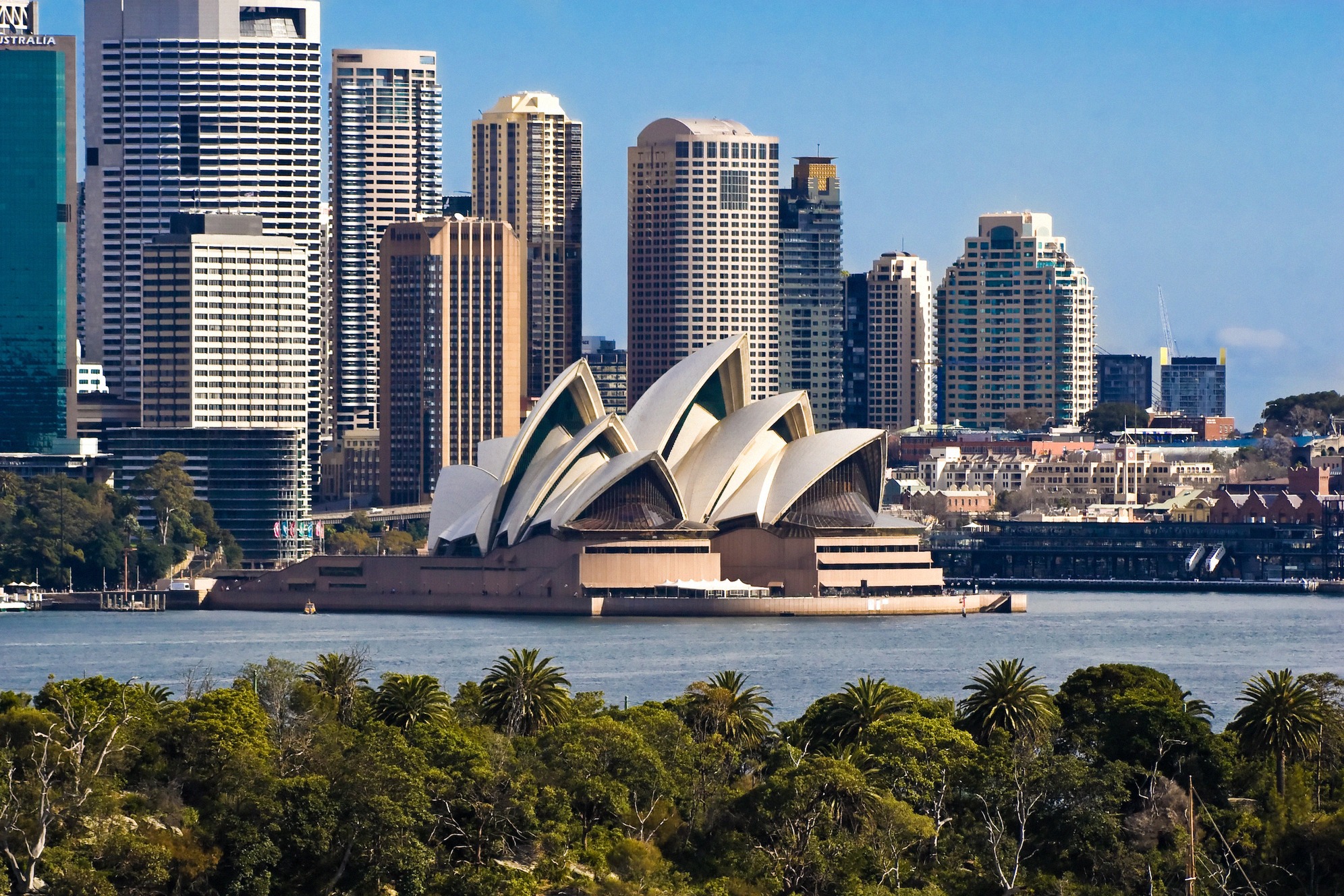 Sydneyn oopperatalo ja taustalla keskustan pilvenpiirtäjät, kuvattuna Sydneyn sataman vastarannalta, Australian tunnetuin maamerkki.