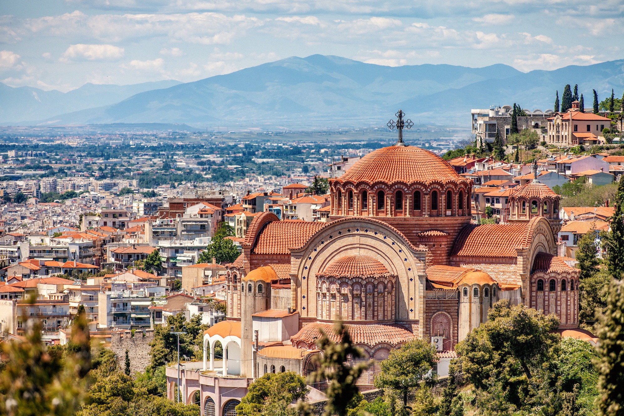 Panoraamanäkymä Thessalonikiin, etualalla näyttävä Pyhän Paavalin kirkko (Agios Pavlos), bysanttilaisvaikutteinen punatiilinen kupolirakennus, taustalla levittäytyvä kaupunki ja Makedonian vuoret.
