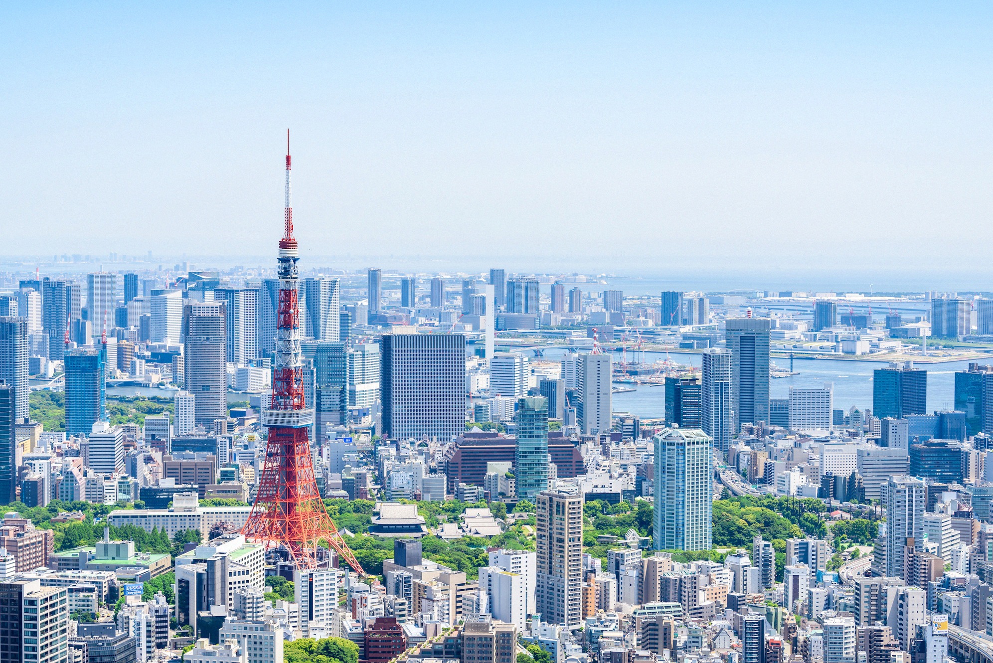 Henkeäsalpaava alkukesän näkymä Tokion silhuetille, keskellä puna-valkoinen Tokyo Tower, takana satama, Rainbow Bridge ja loputon kaupunkialue.