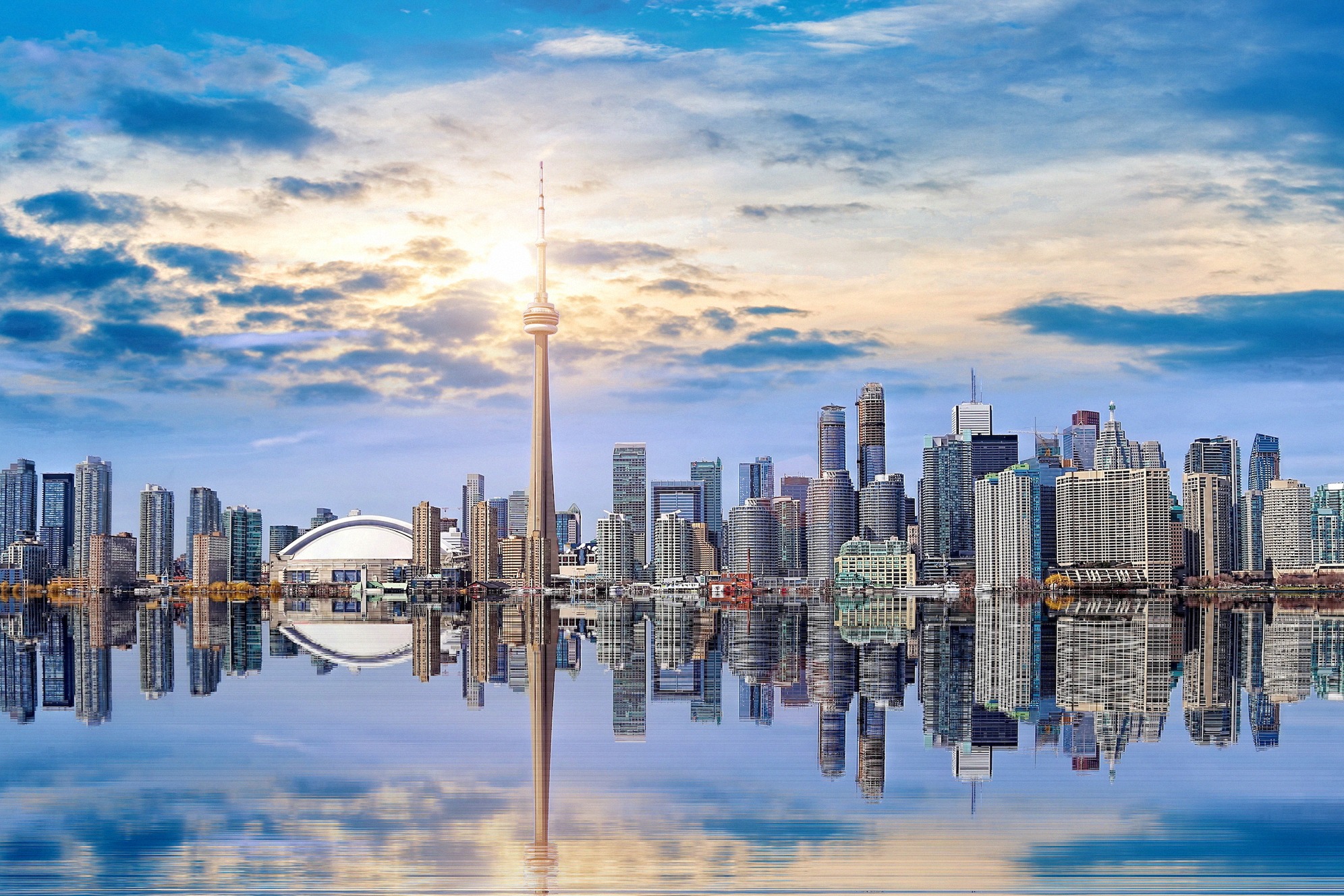 Toronton ikoninen silhuetti Ontariojärveltä auringonlaskussa: CN Tower hallitsee siluettia, joka heijastuu maalauksellisesti tyyneen veteen.