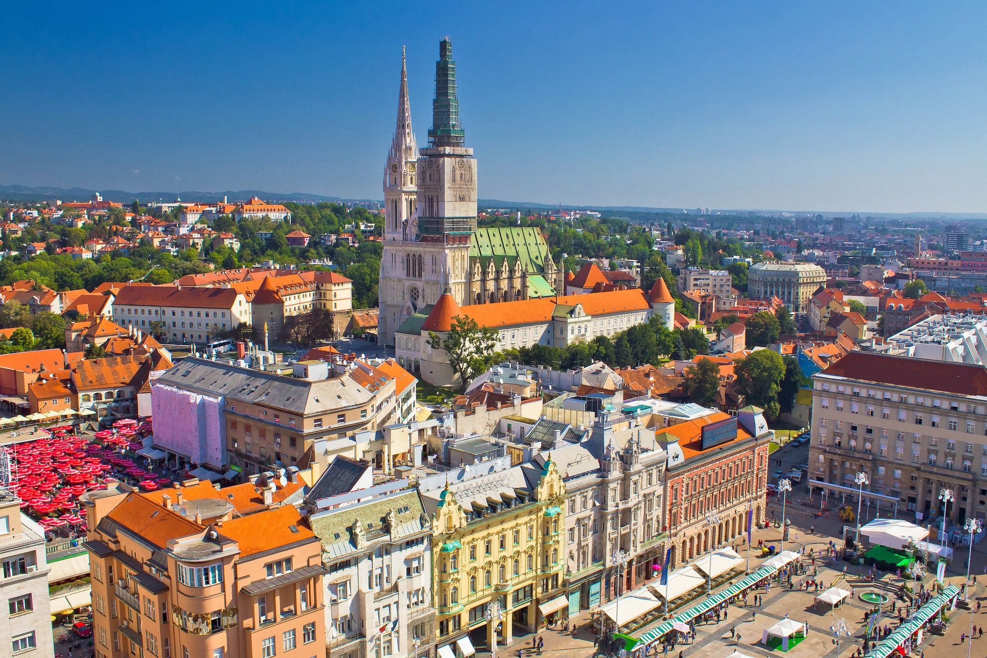 Ilmakuva Zagrebista, jossa näkyvät Ban Jelačićin aukio ja goottilainen tuomiokirkko tunnistettavine kaksoistorneineen - etualalla toripäivänvarjoja ja komeita 1800-luvun rakennuksia.